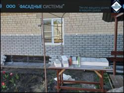 Процесс обшивки стены дома термопанелями из фибробетона в сером цвете под кирпич